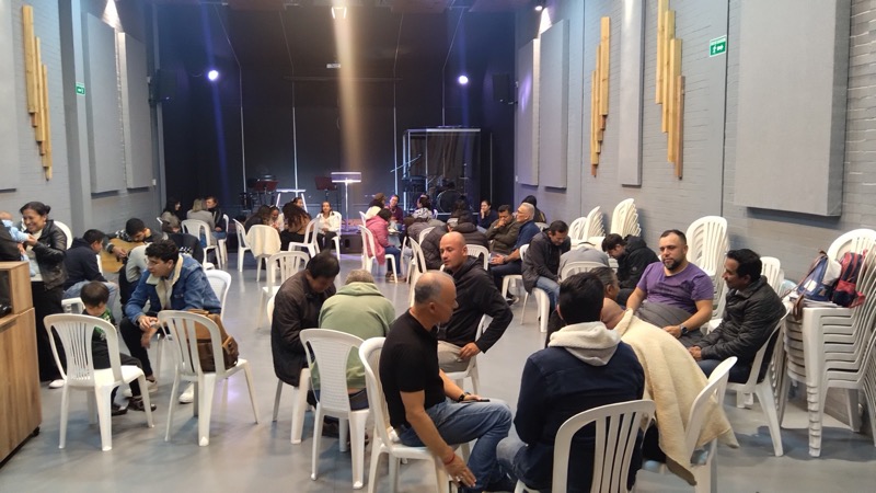 Pequeños grupos conversando en sillas dispuestas en círculos dentro del salón de la iglesia durante el discipulado Nueva Vida en Cristo.