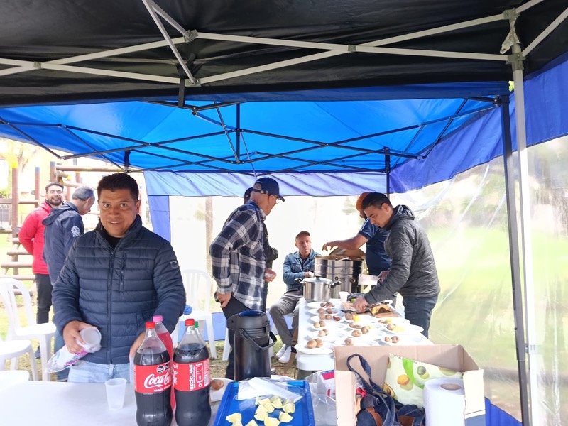 Hombres de la iglesia compartiendo comida bajo una carpa al aire libre durante un encuentro del grupo de varones.